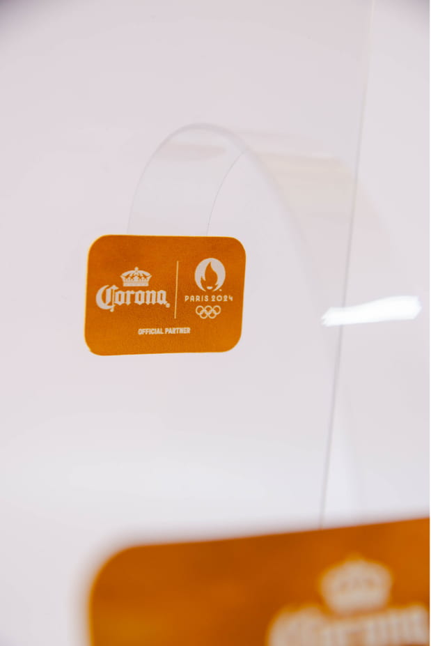 Mini wobbler Corona Paris 2024 Official Partner com haste transparente, produzido pela RM2 Holding